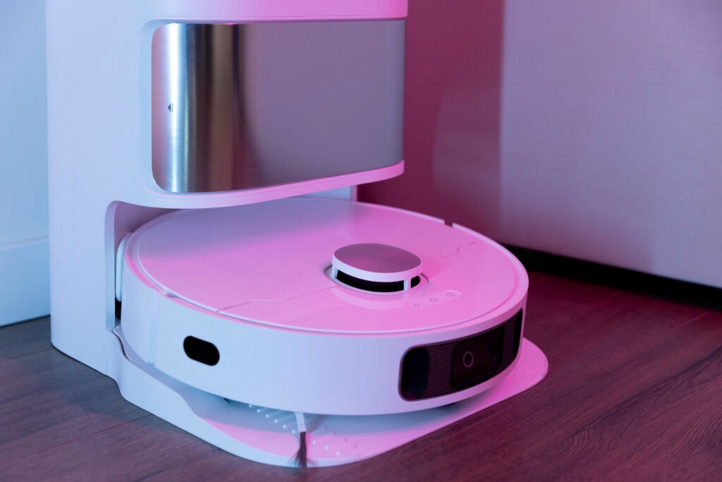 Robô aspirador branco com sensor a laser acoplado à estação de autoesvaziamento, sobre piso de madeira
